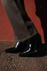 Botín estilo cowboy de caña baja, confeccionado en material sintético con acabado liso. Presenta un diseño de punta fina, tacón curvo en bloque y cierre mediante cremallera lateral.