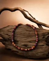Collar artesanal compuesto por cuentas de concha Spóndylus talladas a mano en diversas formas y tonalidades cálidas, que van desde el púrpura y naranja hasta el blanco. Presenta un diseño asimétrico con cierre metálico.