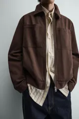 Sobrecamisa de corte regular confeccionada en tejido con estructura canvas color marrón. Presenta un ligero acolchado interior, cuello de solapa y cierre frontal con cremallera metálica. Incluye dos bolsillos de plastrón en el pecho y bolsillos laterales de vivo, con mangas largas terminadas en puños con botón.