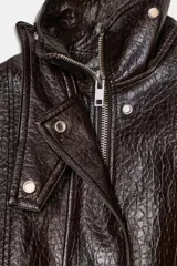 Chaqueta de cuero sintético con textura rugosa, cuello alto con trabilla, cierre frontal con cremallera y botones a presión, bolsillos delanteros y bajo ajustable con hebilla metálica.