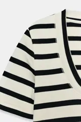 Camiseta de manga corta confeccionada en tejido de algodón con textura rib. Presenta un diseño a rayas horizontales en color blanco y negro, con un escote redondo pronunciado y bajo recto.