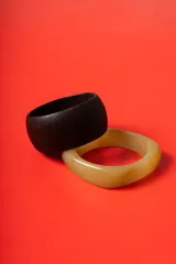 Set de dos brazaletes rígidos, uno de madera oscura con acabado mate y otro de resina en tono beige marmolado.