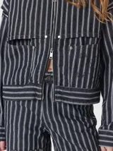 Campera de denim a rayas verticales con cuello de pana en color bordó. Presenta cierre frontal, mangas desmontables con cierre en los hombros, canesú en el pecho y bolsillos de parche cuadrados.