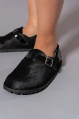 Zuecos negros con textura de pelo, hebilla plateada y suela plana.