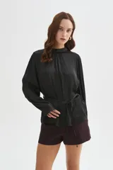 Blusa de poliéster color negro con cuello alto, mangas largas, diseño holgado, detalles de frunces y lazo ajustable en la cintura.