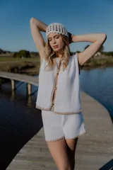 Conjunto de dos piezas tejido en algodón, compuesto por un chaleco sin mangas con cierre frontal de botones y un short de tiro medio. Ambas prendas presentan un diseño en color blanco con detalles de terminaciones en color beige.