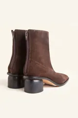 Bota de caña media confeccionada en cuero vacuno negro, con diseño minimalista y cierre trasero. Presenta un taco cilíndrico de madera tallada y punta cuadrada.