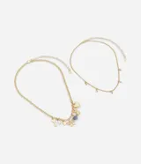 Collar de dos capas en metal con baño dorado. La primera capa presenta una cadena mediana con dijes variados que incluyen un corazón, un osito, un corazón de resina, un lazo, un candado, una llave y una perla. La segunda capa consiste en una cadena más fina con pequeños dijes ovalados de cristal distribuidos a lo largo.
