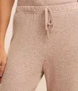 Conjunto de pijama de tres piezas confeccionado en tricot, compuesto por una blusa de cuello redondo, un pantalón de corte recto con cintura elástica y una bata larga abierta. Presenta una textura suave y fluida en color beige.