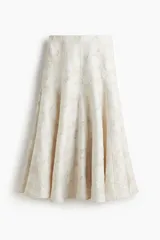 Pollera midi de tiro alto, corte circular con volumen y vuelo, confeccionada en tejido jacquard color blanco roto con textura. Posee forro interior y cierre oculto con corchete en la parte trasera.