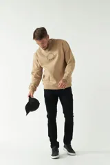 Buzo de felpa color beige con cuello redondo, manga larga y puños acanalados. Presenta un logo circular estampado en el frente.