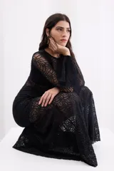 Vestido largo de encaje negro con transparencias, corte ajustado al cuerpo, mangas largas con terminación acampanada y falda con caída fluida.