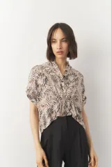 Blusa corta de manga corta con estampado en blanco y negro, cuello mao y cierre frontal con botones. Cuenta con detalle de elástico fruncido en la cintura que genera un efecto peplum.