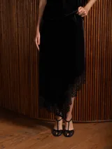 Pollera midi de terciopelo negro con corte asimétrico y detalle de encaje en el ruedo.