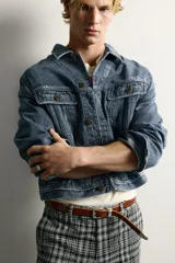 Campera de denim de algodón en color azul, con lavado efecto desgastado, cuello solapa y cierre frontal de botonadura metálica. Presenta bolsillos con solapa en el pecho, mangas largas con puños abotonados y trabilla ajustable en la cintura posterior.