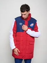 Parka larga de abrigo Umbro del Club Nacional de Football, con diseño tricolor en rojo, azul y blanco. Presenta cuello alto, cierre frontal con solapa, bolsillos con cierre en el pecho y logo de la marca junto al escudo del club.