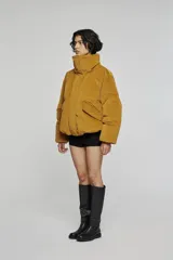 Chaqueta acolchada de corte corto y volumen amplio, color verde oscuro. Presenta cuello alto envolvente, cierre frontal con cremallera oculta, bolsillos laterales integrados y mangas de línea amplia.