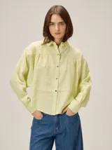Camisa de lino color verde lima, con cuello clásico, cierre frontal de botones y mangas largas con puños. Presenta detalles de pespuntes en zigzag en la zona de los hombros y canesú.