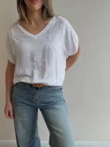 Blusa blanca de corte relajado, con escote en V, mangas cortas amplias y detalles de bordados florales en relieve.
