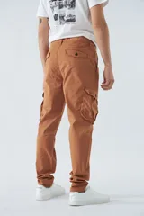 Pantalón cargo color beige, corte slim, con cierre y botón en la cintura, pasacintos, bolsillos cargo con botones y sin puños.