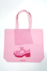 Bolso tote de tela color rosado con diseño gráfico estampado en contraste que simula una falda a cuadros y un zapato de plataforma con estrellas, además del logotipo de la marca Indian.