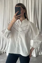 Camisa negra de manga larga con diseño abullonado, cuello clásico y cierre frontal de botones. Presenta detalles de alforzas y encaje en la parte superior delantera.