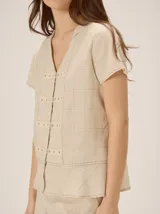 Camisa de manga corta color beige con estampado a cuadros, cuello en V y detalles de galones decorativos estilo oriental en la parte frontal.