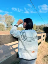 Sweater de punto en color marrón con diseño jacquard geométrico en blanco y gris en cuello, puños y pecho. Presenta cuello redondo, mangas largas y corte holgado.