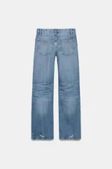 Jeans de tiro bajo y cinco bolsillos, con diseño de pierna ancha y larga. Presenta roturas y desgastes sutiles en la parte delantera. Cierre frontal con cremallera y botón metálico.