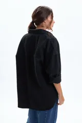 Sobrecamisa de jean color negro, con corte oversize, cuello camisero, cierre frontal con botones metálicos y bolsillos frontales con solapa.