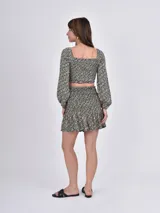 Blusa corta con estampado floral en tonos beige y negro, escote cuadrado y mangas largas abullonadas con puños elásticos.