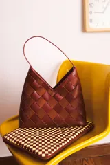 Cartera de cuero trenzado a mano, con forro interior y asa corta. Diseño con patrón de tablero en tonos marrones.