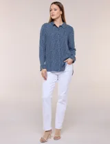 Camisa de rayón azul marino con estampado de lunares pequeños en tonos claros, cuello camisero, cierre frontal de botones, mangas largas y ruedo curvo asimétrico más largo en la espalda.