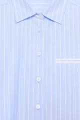 Camisa de manga larga, corta (crop), con cuello solapa y bolsillo de vivo en el delantero. Presenta un patrón de rayas verticales azules y blancas, con detalles de acabado en blanco en los puños y el bolsillo.