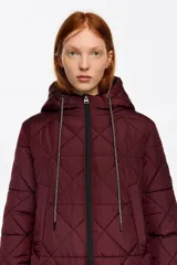 Abrigo largo de corte recto confeccionado en tejido técnico acolchado con diseño de rombos, cierre frontal con cremallera, cuello subido con capucha integrada, manga larga con puño elástico y bolsillos laterales.