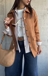 Chaqueta de gamuza color camel, con corte recto, cuello camisero, cierre frontal con botones metálicos y bolsillos frontales con solapa.