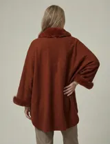 Ruana tejida color terracota, de corte amplio y asimétrico, con cuello y puños adornados con apliques de piel sintética del mismo tono.