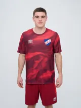 Remera de entrenamiento Umbro del Club Nacional de Football, modelo Press, para hombre. Diseño en tonos de rojo con patrón estampado tipo humo o abstracto, cuello redondo y mangas cortas. Incluye el logo de Umbro y el escudo del club en el pecho.