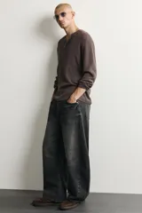 Jeans de denim de algodón color gris con efecto lavado, de corte relaxed barrel fit y tiro medio. Presenta diseño amplio con pinzas en las rodillas y costuras curvas, cierre frontal con botones y cinco bolsillos tradicionales.