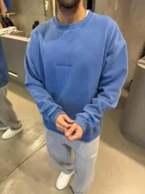 Buzo de algodón en color azul con efecto lavado, cuello redondo y puños acanalados. Presenta un diseño minimalista con el logo de la marca bordado en el centro del pecho.