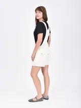 Monoprenda corta estilo overol de jean color beige, con bolsillos frontales, tirantes ajustables con hebillas metálicas y short con vuelta en el dobladillo.