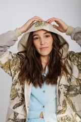 Canguro con capucha y cierre frontal, color beige con estampado de hojas en tonos marrones y amarillos. Mangas largas en color gris.