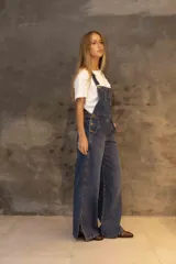 Enterito de denim azul con silueta relajada, breteles regulables, peto con bolsillo frontal y piernas rectas con tajos laterales en el ruedo.