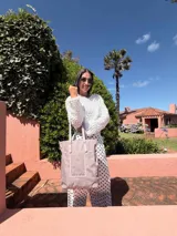 Bolso tipo tote bag de símil cuero color rosa pálido, con asas dobles y detalles de costura en color beige claro. Presenta un bolsillo frontal rectangular aplicado y herrajes metálicos.