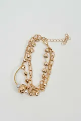Brazalete multicapa color dorado, compuesto por cadenas de diferentes eslabones, dijes en forma de corazón y detalles de perlas blancas.