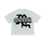 Camiseta blanca de manga corta con gran estampado frontal de estilo urbano que incluye la palabra "Emotion" en letras estilo grafiti con efecto brillante y una ilustración de dos niños con alas de ángel en un taller mecánico junto a un avión azul.