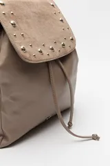 Mochila negra de símil cuero texturizado con tapa en acabado gamuzado, decorada con apliques de tachas metálicas. Tiene asa superior y correas regulables.