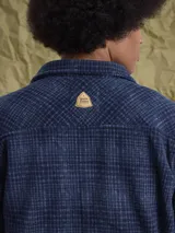 Sobrecamisa de tejido polar con estampado abstracto en tonos rojizos y azul marino. Presenta cuello clásico, cierre frontal con botones a presión, dos bolsillos frontales con solapa en el pecho y un parche decorativo.