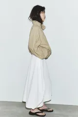 Falda midi blanca de tiro medio con bolsillos delanteros y bajo asimétrico. Cierre lateral con cremallera oculta.