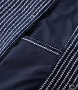 Campera masculina de corte recto con textura jacquard a rayas verticales en tonos azul marino y blanco. Presenta cuello inglés, cierre frontal con botones y manga larga.